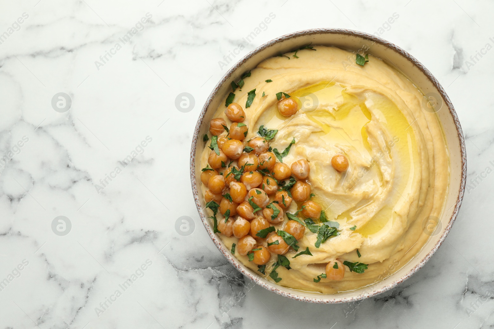 Photo of Delicious hummus with olive oil, chickpeas and parsley in bowl on white marble table, top view. Space for text