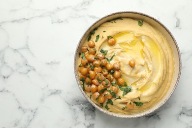 Photo of Delicious hummus with olive oil, chickpeas and parsley in bowl on white marble table, top view. Space for text