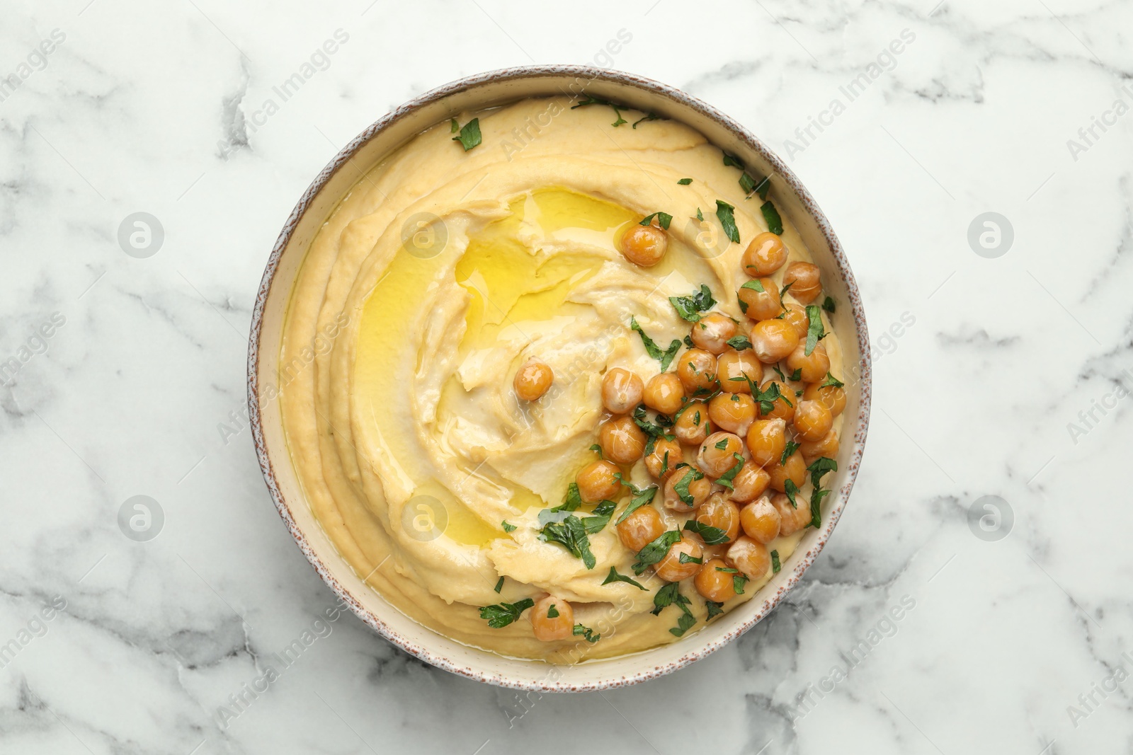 Photo of Delicious hummus with olive oil, chickpeas and parsley in bowl on white marble table, top view