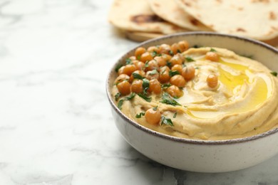 Photo of Delicious hummus with olive oil, chickpeas and parsley in bowl on white marble table, closeup. Space for text