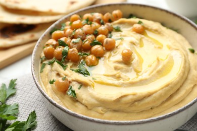 Photo of Delicious hummus with olive oil, chickpeas and parsley in bowl on table, closeup