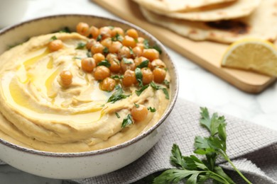 Photo of Delicious hummus with olive oil, chickpeas and parsley in bowl on table, closeup