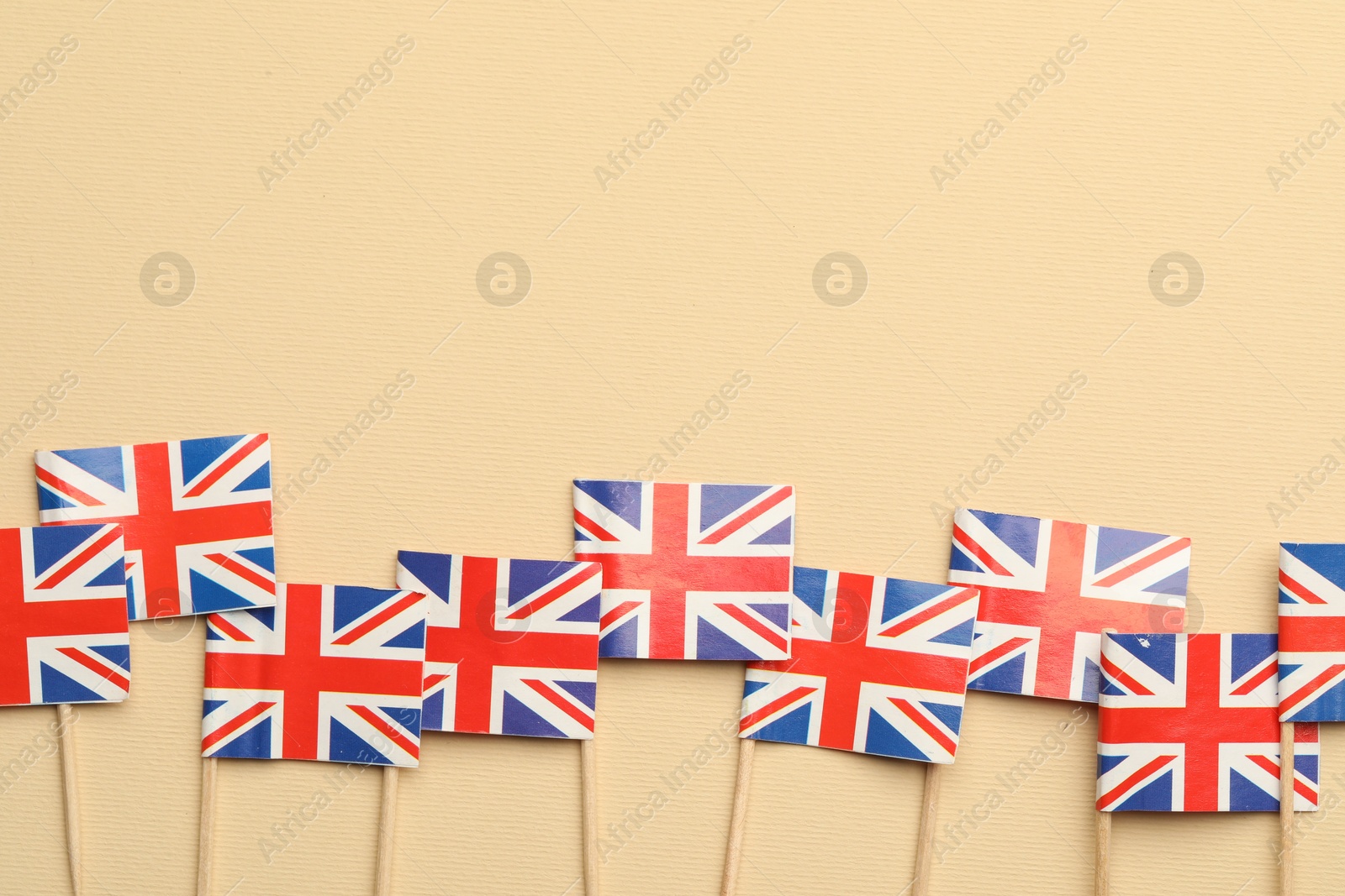 Photo of Small paper flags of United Kingdom on beige background, top view. Space for text