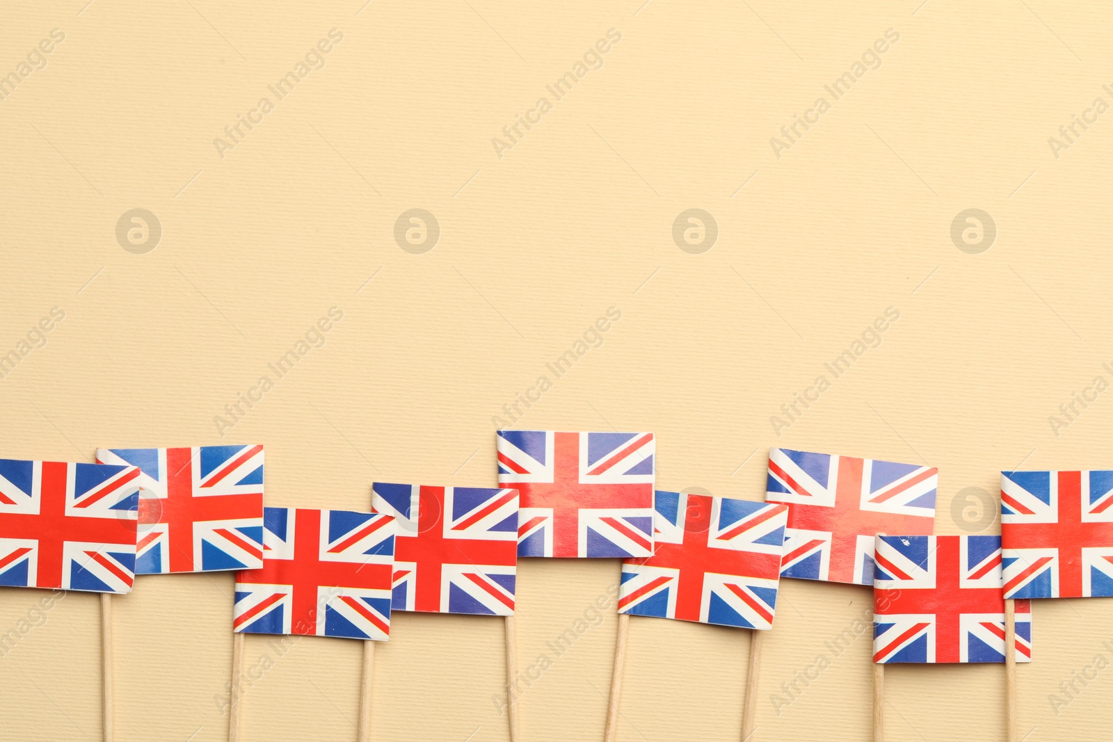 Photo of Small paper flags of United Kingdom on beige background, top view. Space for text