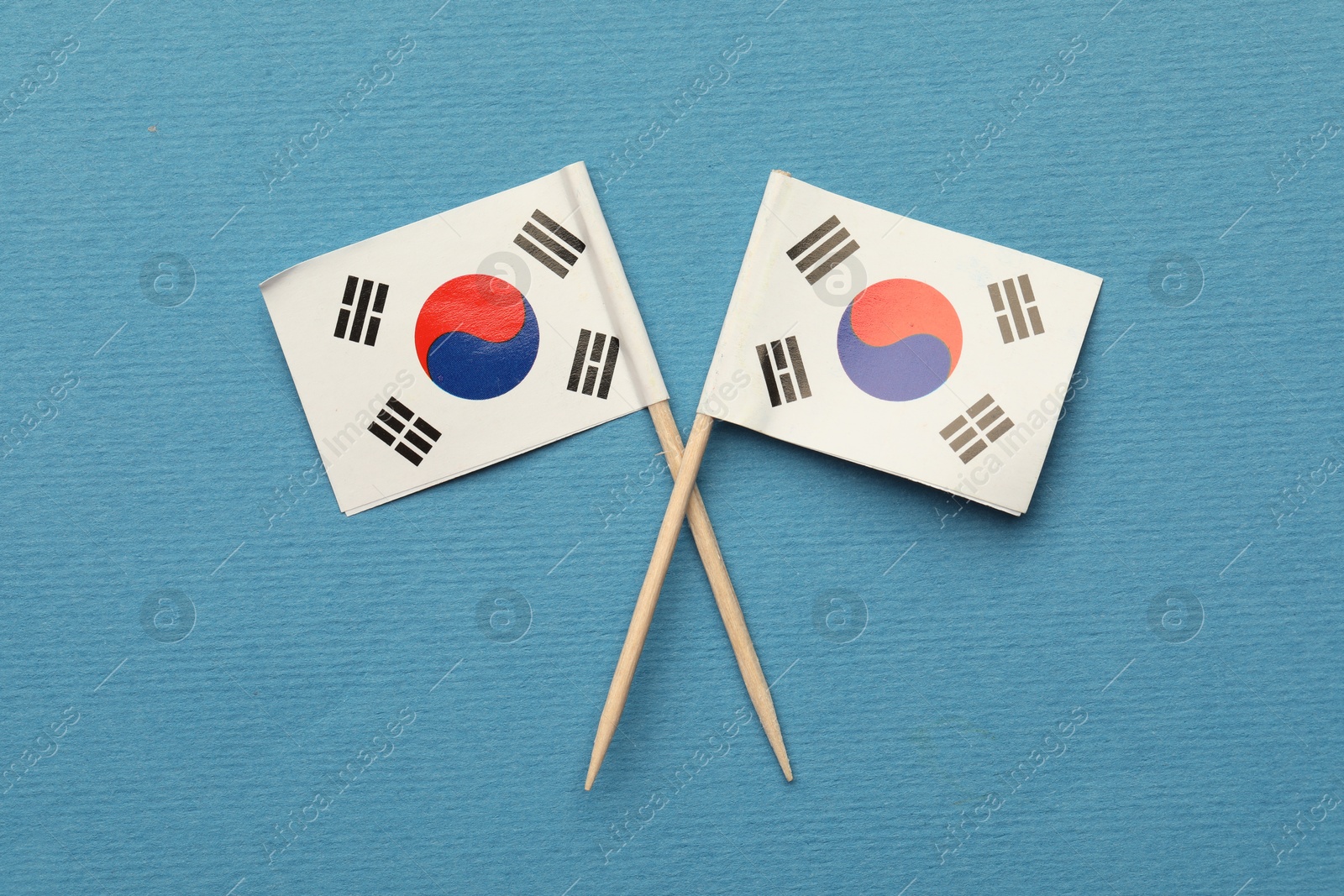 Photo of Small paper flags South Korea on light blue background, top view