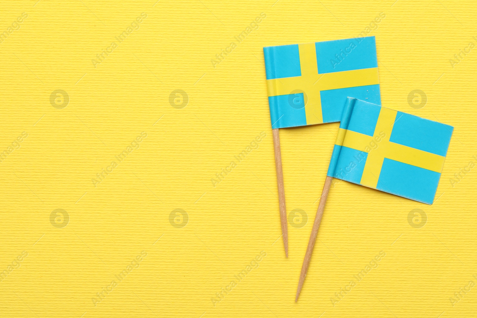 Photo of Small paper flags of Sweden on yellow background, top view. Space for text