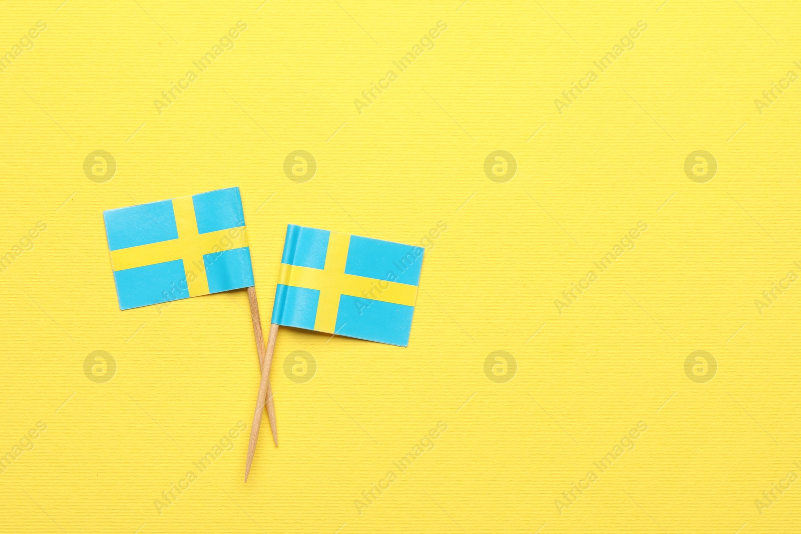 Photo of Small paper flags of Sweden on yellow background, top view. Space for text