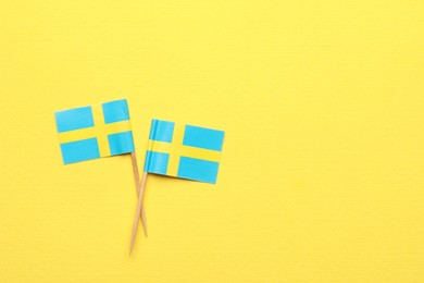 Small paper flags of Sweden on yellow background, top view. Space for text