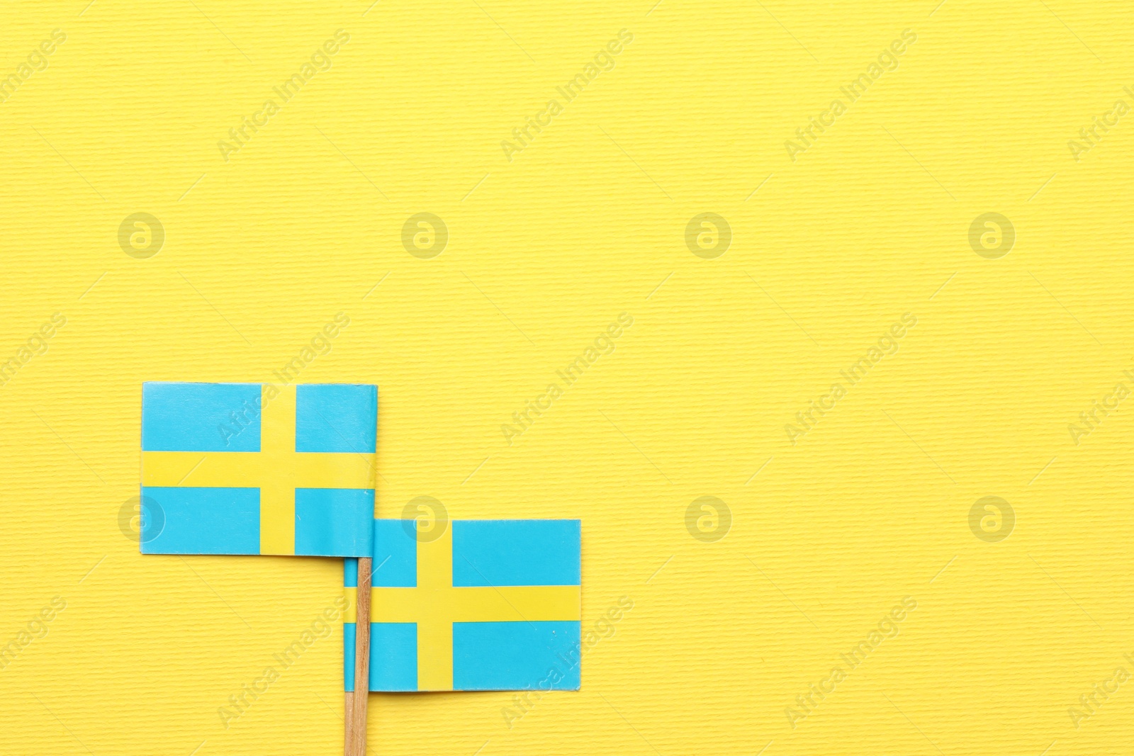 Photo of Small paper flags of Sweden on yellow background, top view. Space for text