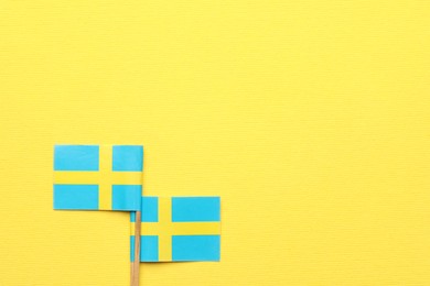 Small paper flags of Sweden on yellow background, top view. Space for text