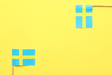 Small paper flags of Sweden on yellow background, top view. Space for text