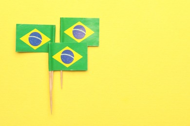 Photo of Small paper flags of Brazil on yellow background, top view. Space for text