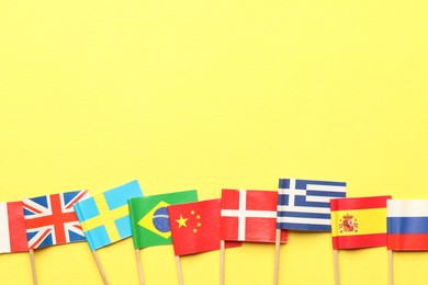 Photo of Small paper flags of different countries on yellow background, flat lay. Space for text