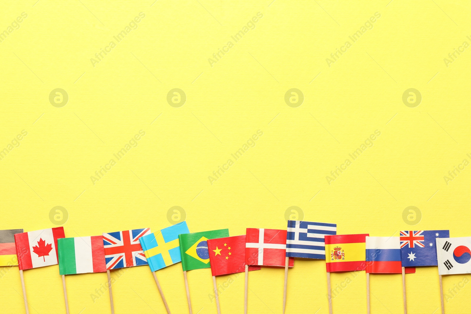 Photo of Small paper flags of different countries on yellow background, flat lay. Space for text