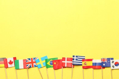 Small paper flags of different countries on yellow background, flat lay. Space for text