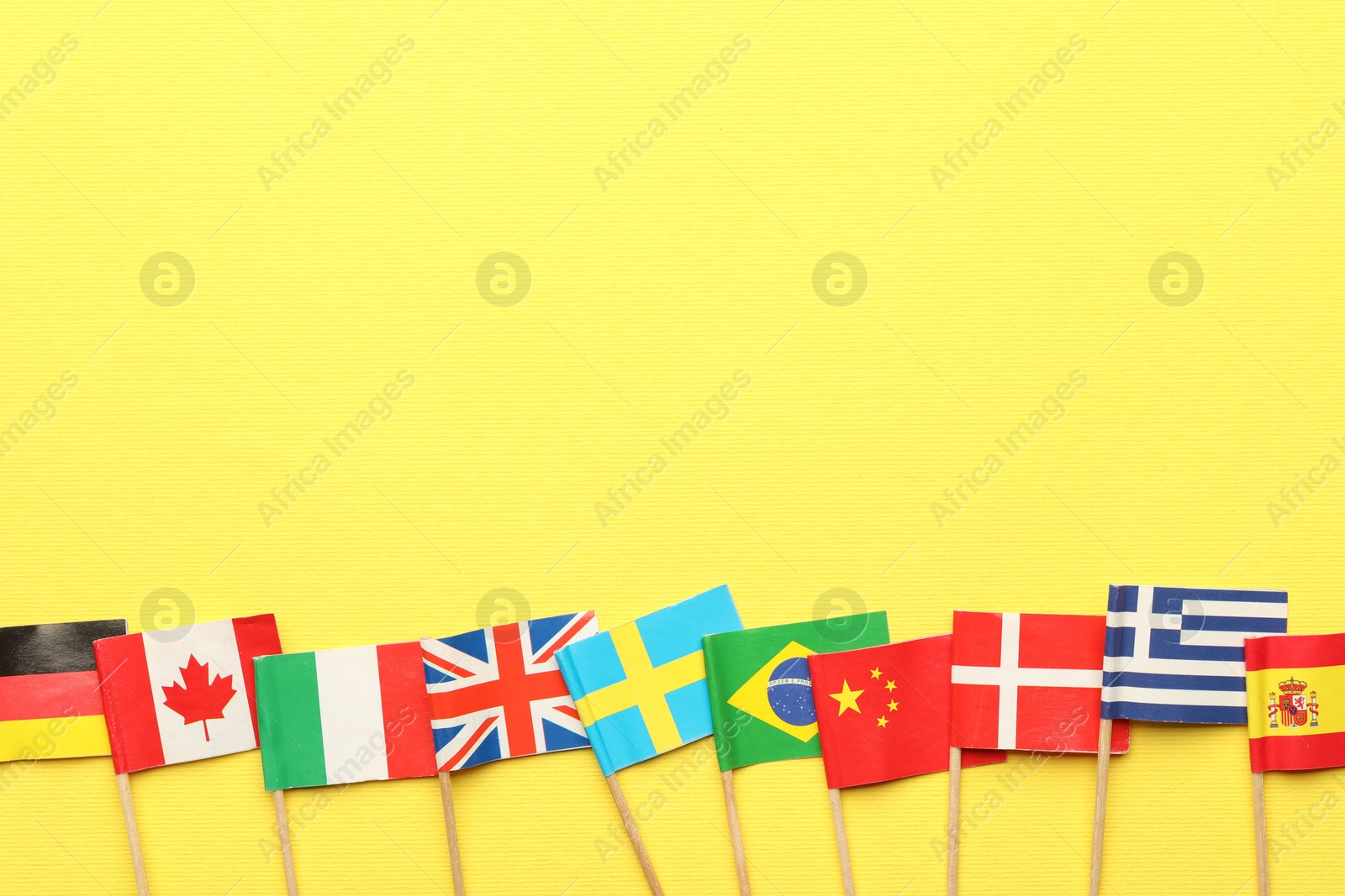 Photo of Small paper flags of different countries on yellow background, flat lay. Space for text