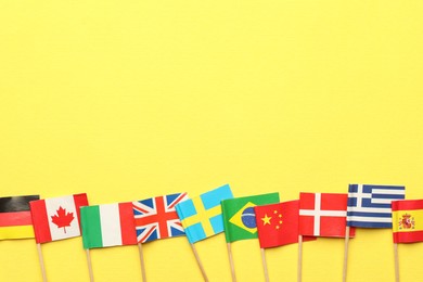 Small paper flags of different countries on yellow background, flat lay. Space for text