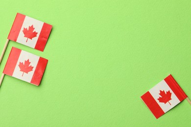 Small paper flags of Canada on green background, top view. Space for text