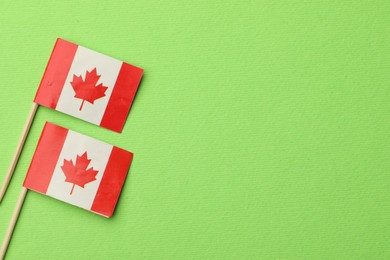 Small paper flags of Canada on green background, top view. Space for text