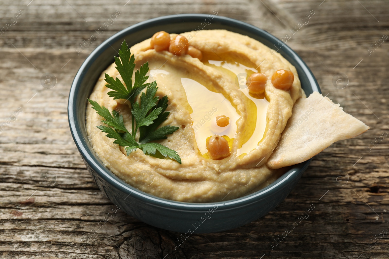 Photo of Delicious hummus with olive oil, chickpeas and pita in bowl on wooden table, closeup