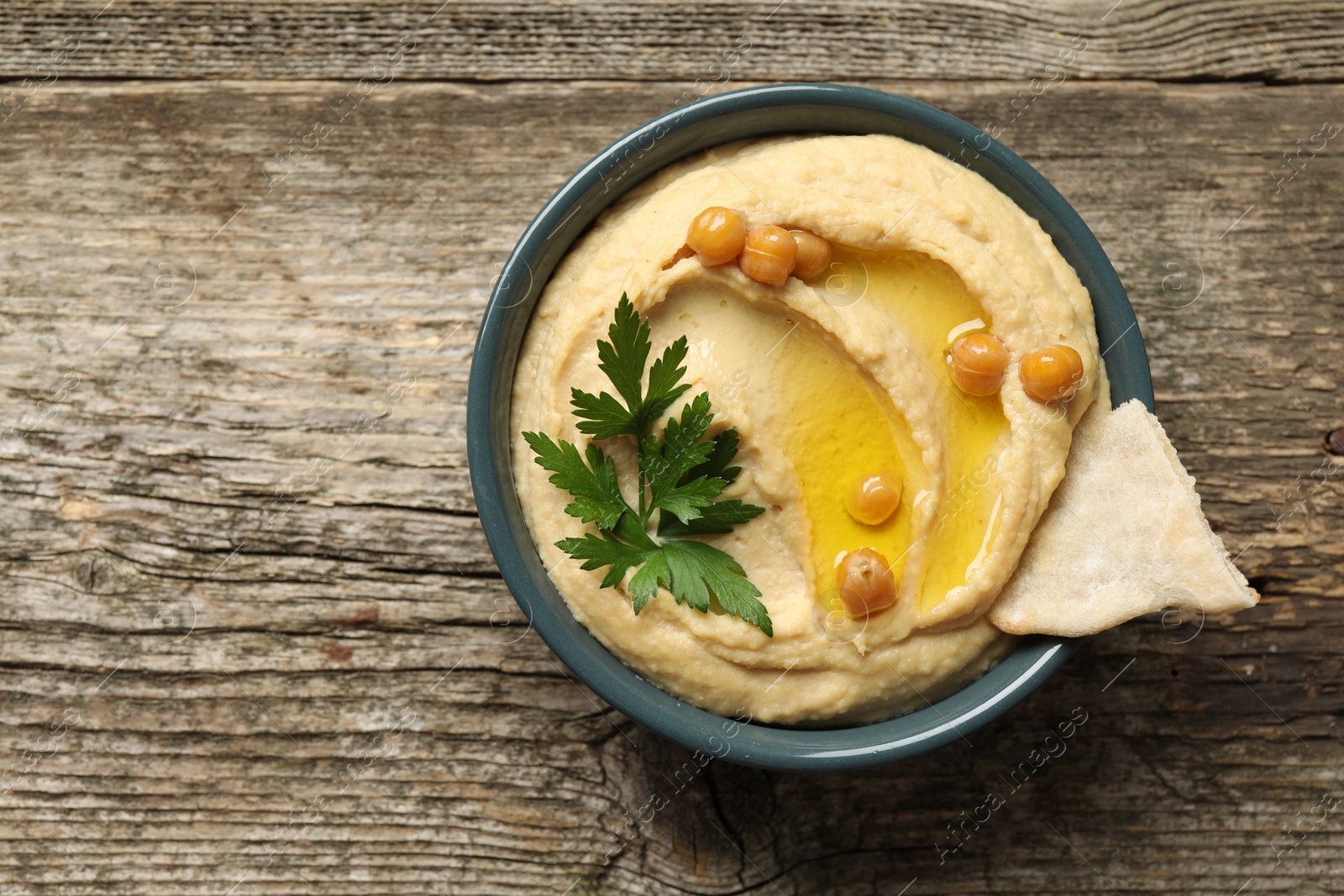 Photo of Delicious hummus with olive oil, chickpeas and pita in bowl on wooden table, top view