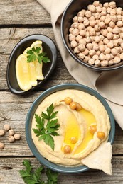 Photo of Delicious hummus with olive oil, chickpeas, lemon and pita on wooden table, flat lay