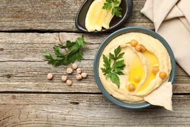 Photo of Delicious hummus with olive oil, chickpeas, lemon and pita on wooden table, flat lay