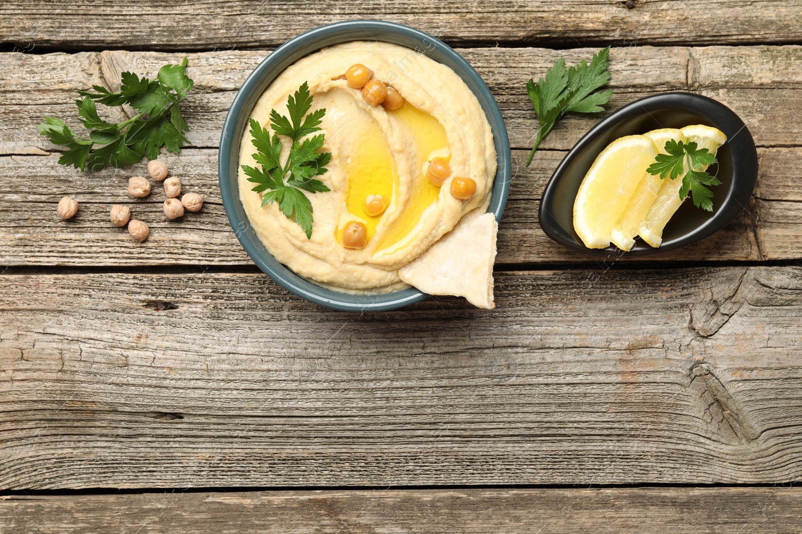 Photo of Delicious hummus with olive oil, chickpeas, lemon and pita on wooden table, flat lay. Space for text