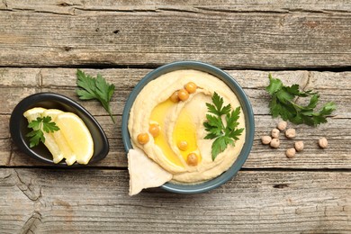 Delicious hummus with olive oil, chickpeas, lemon and pita on wooden table, flat lay