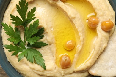 Photo of Delicious hummus with olive oil, chickpeas, parsley and pita in bowl, top view