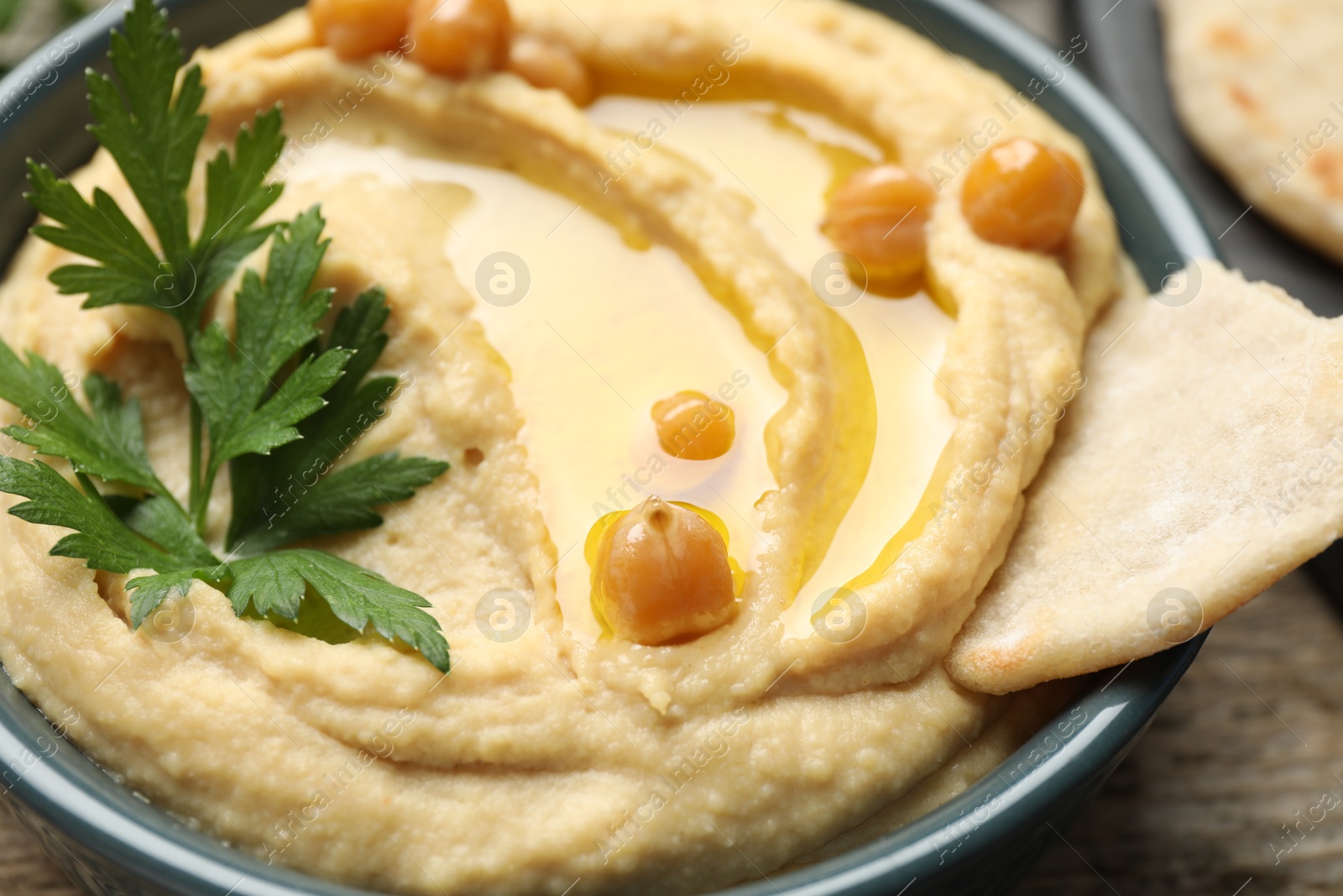 Photo of Delicious hummus with olive oil, chickpeas, parsley and pita in bowl on table, closeup