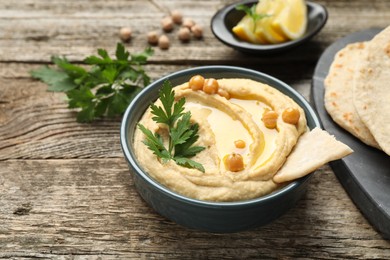 Photo of Delicious hummus with olive oil, chickpeas, parsley and pita in bowl on wooden table