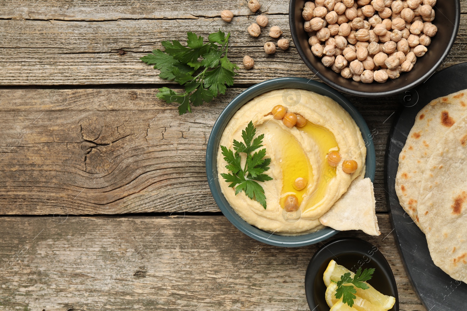 Photo of Delicious hummus with olive oil, chickpeas, lemon and pita on wooden table, flat lay. Space for text