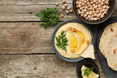 Delicious hummus with olive oil, chickpeas, lemon and pita on wooden table, flat lay. Space for text