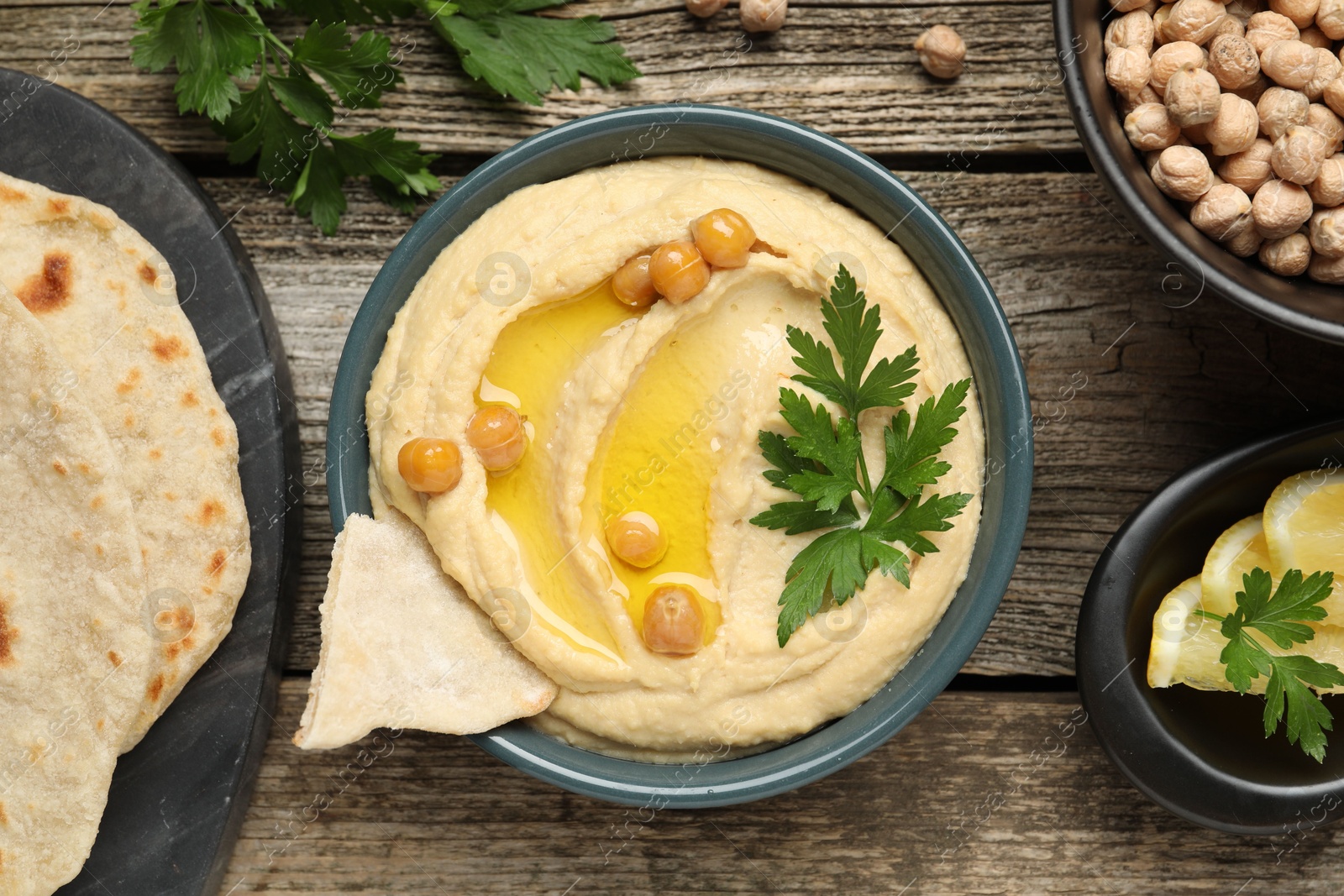 Photo of Delicious hummus with olive oil, chickpeas, lemon and pita on wooden table, flat lay