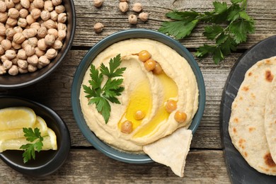 Photo of Delicious hummus with olive oil, chickpeas, lemon and pita on wooden table, flat lay