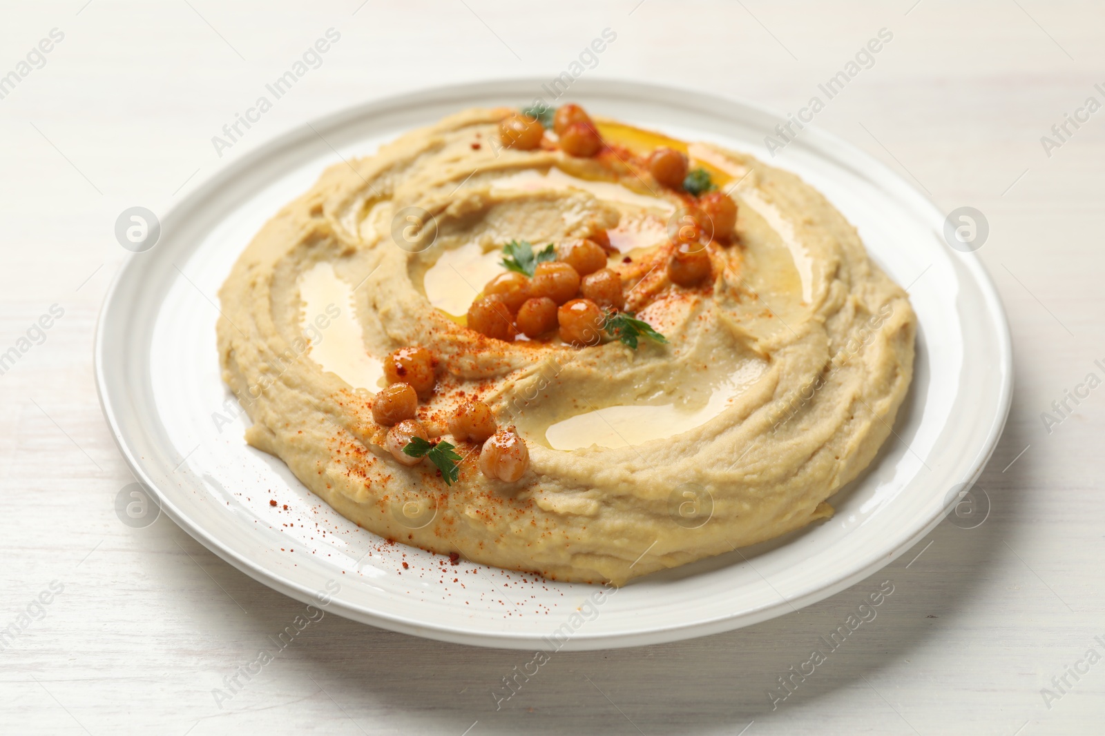 Photo of Delicious hummus with olive oil, chickpeas and paprika on white wooden table