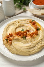 Delicious hummus with olive oil, chickpeas and paprika on white wooden table, closeup