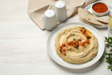 Photo of Delicious hummus with olive oil, chickpeas and paprika served on white wooden table, space for text