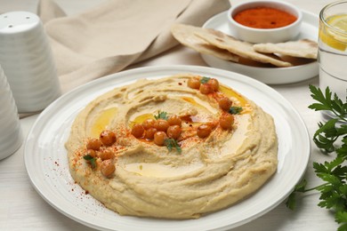 Photo of Delicious hummus with olive oil, chickpeas and paprika served on white wooden table