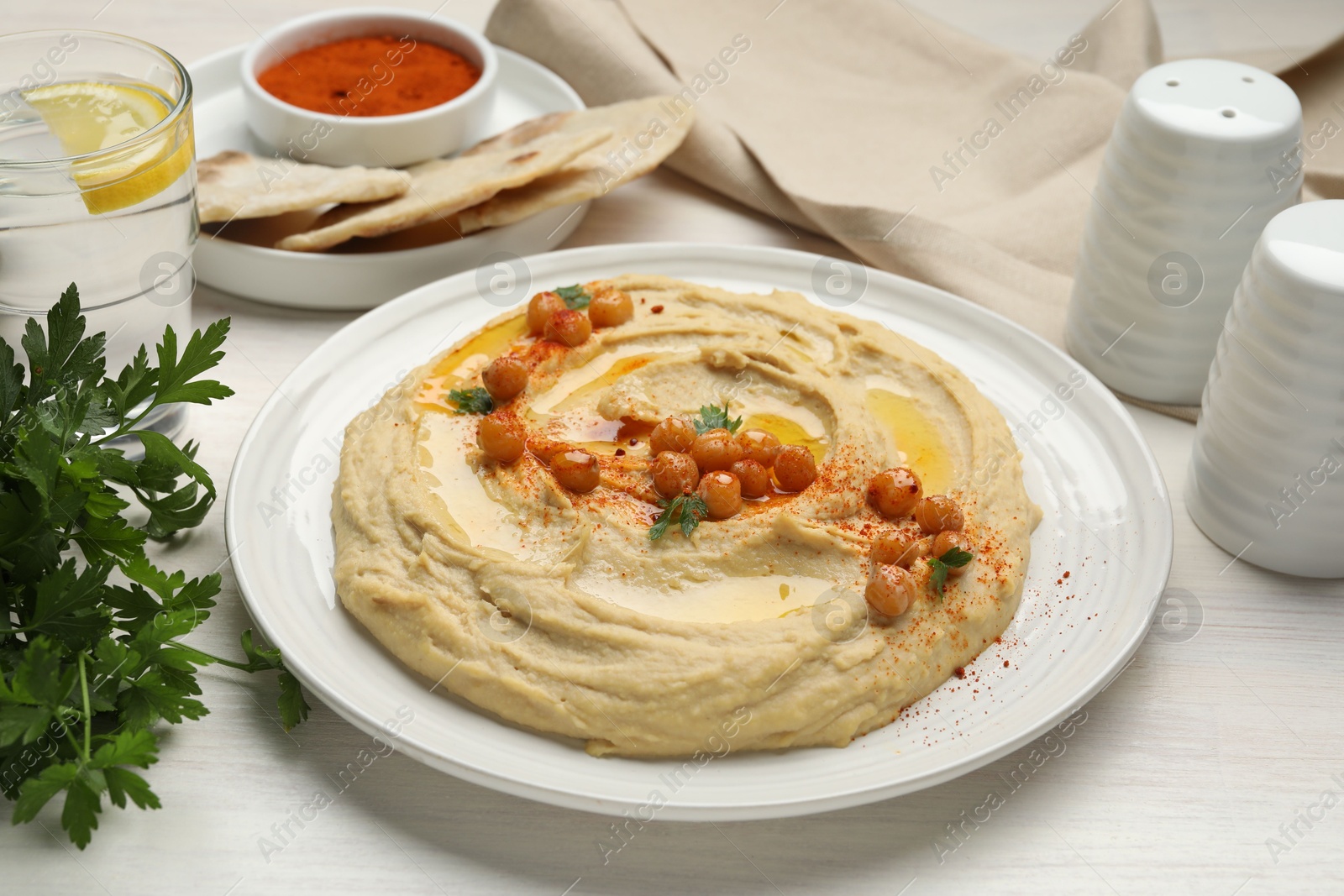 Photo of Delicious hummus with olive oil, chickpeas and paprika served on white wooden table