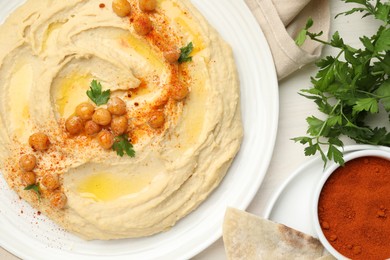 Photo of Delicious hummus with olive oil, chickpeas and paprika served on white wooden table, flat lay