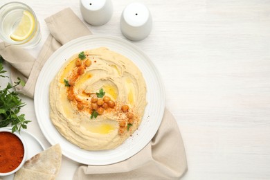 Photo of Delicious hummus with olive oil, chickpeas and paprika served on white wooden table, flat lay. Space for text