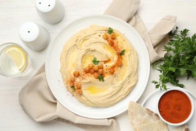 Delicious hummus with olive oil, chickpeas and paprika served on white wooden table, flat lay