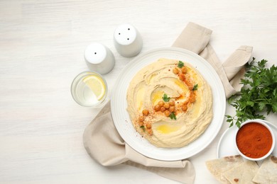 Photo of Delicious hummus with olive oil, chickpeas and paprika served on white wooden table, flat lay