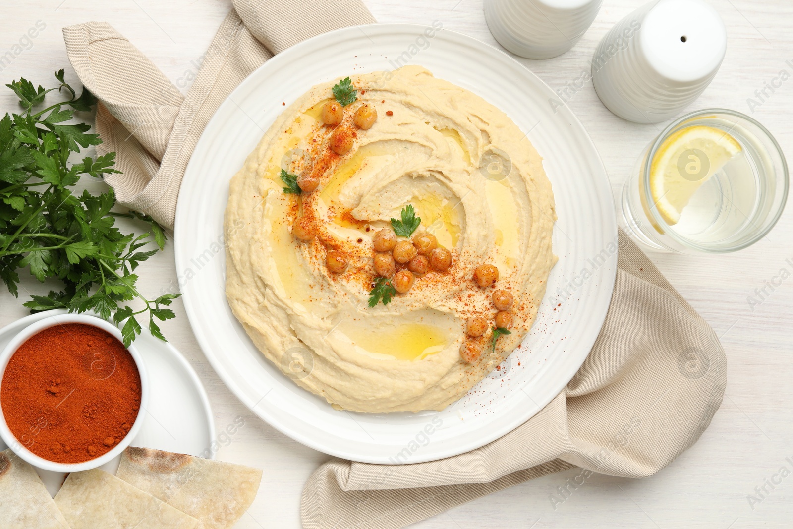 Photo of Delicious hummus with olive oil, chickpeas and paprika served on white wooden table, flat lay