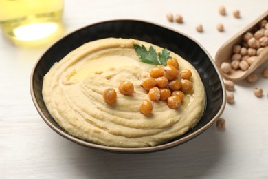 Delicious hummus with olive oil, chickpeas and parsley in bowl on white wooden table