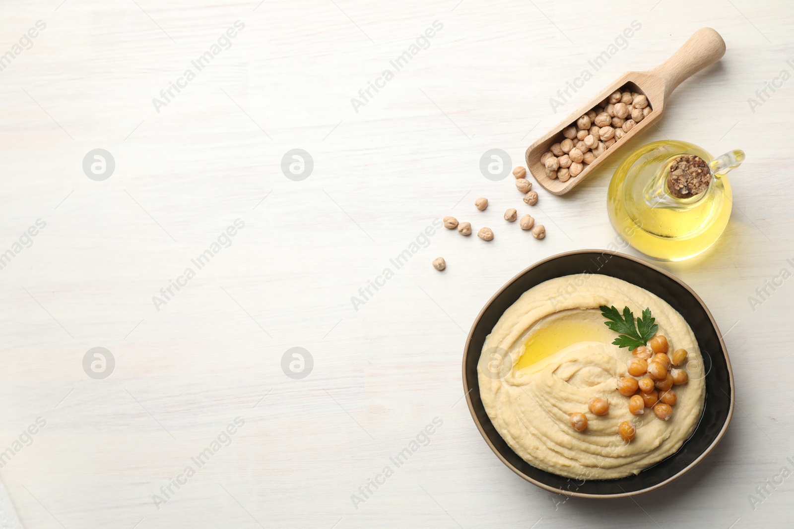 Photo of Delicious hummus with olive oil, chickpeas and parsley on white wooden table, flat lay. Space for text