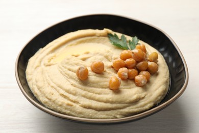 Photo of Delicious hummus with olive oil, chickpeas and parsley in bowl on white wooden table, closeup