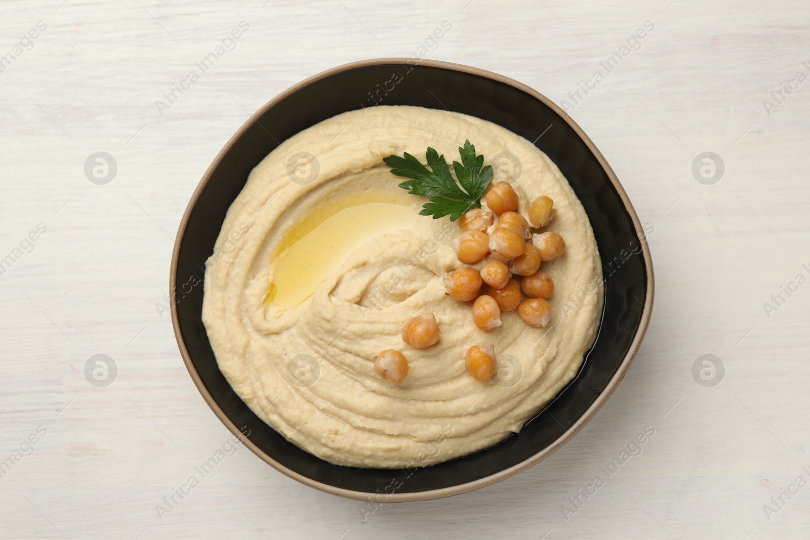 Photo of Delicious hummus with olive oil, chickpeas and parsley in bowl on white wooden table, top view